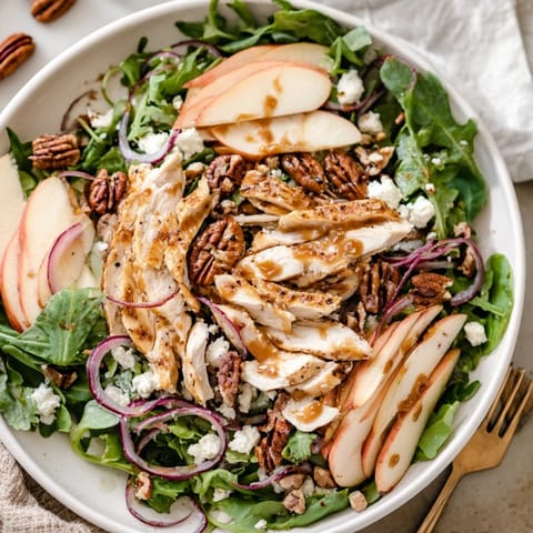 A serving of Caramel Apple Chicken Salad with crumbled goat cheese, dried cranberries, and red onion on a platter, ready to enjoy with a glass of white wine.
