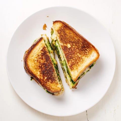 Two halves of a golden spinach pesto grilled cheese sandwich resting on a white plate, showing gooey melted cheese pull.