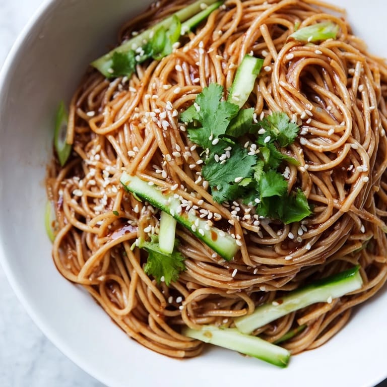 Chilled sesame noodle salad served in a white bowl, topped with toasted peanuts, sesame seeds, and spring onions.