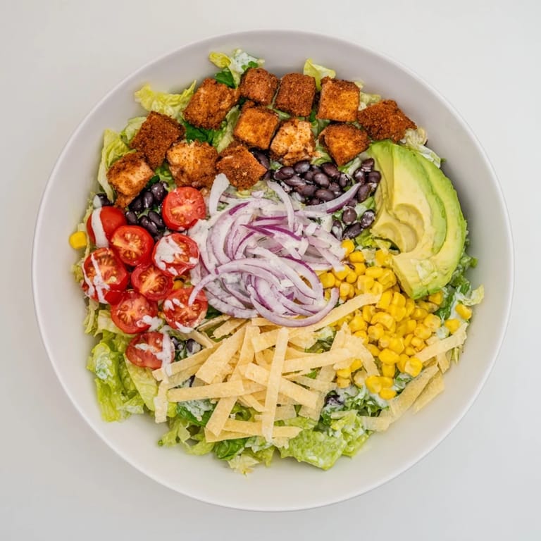 Colorful Tex-Mex Crispy Chicken Taco Salad served in a white bowl, garnished with red onion and ready for a light lunch.
